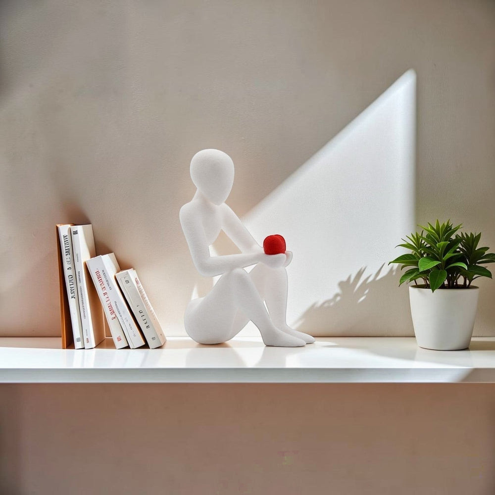Tom GO abstract white figurine holding a red heart, seated in contemplation. Modern decor.