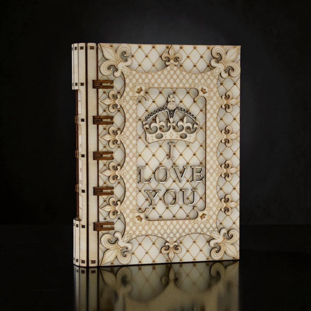 Cutie cadou Tom GO din lemn, în formă de carte, cu mesajul "I LOVE YOU" și o coroană regală, decorată cu motive florale și geometrice.