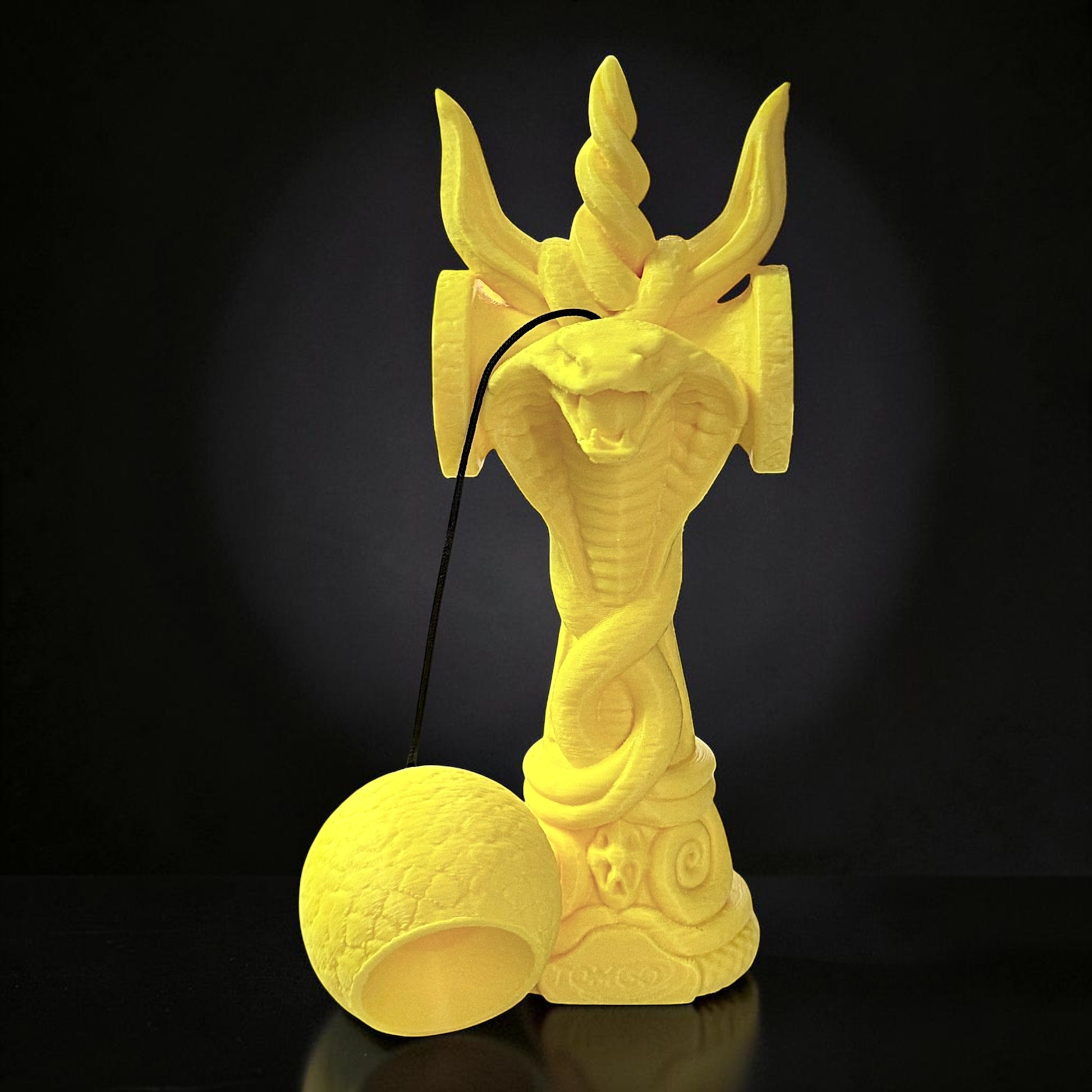 Jucărie Kendama Cobra Tom GO din lemn de fag, galbenă, cu design detaliat de șarpe încolăcit și accesorii pentru joc.