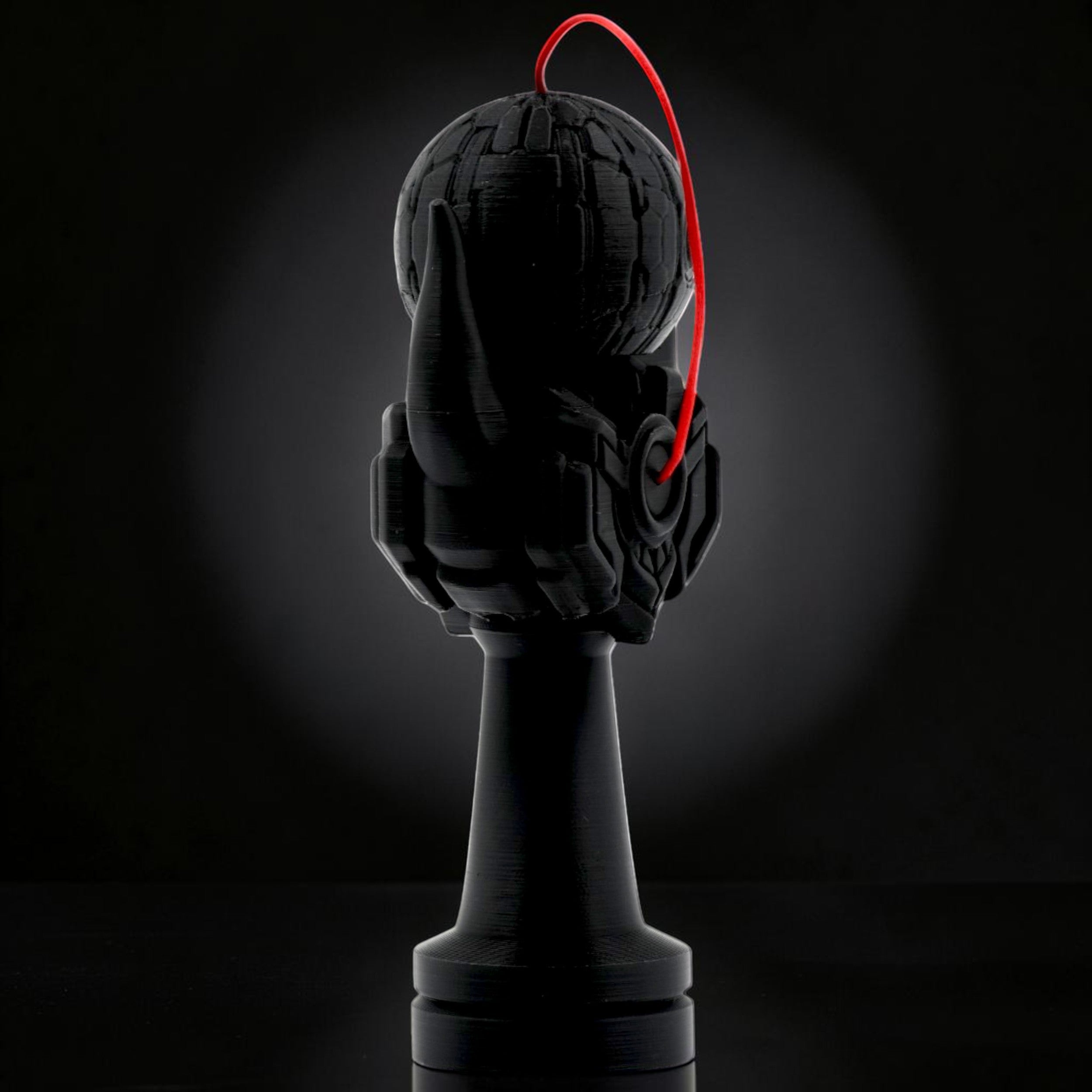 Tom Go Kendama Geeker Iron M black kendama with a red string and intricate hand design.