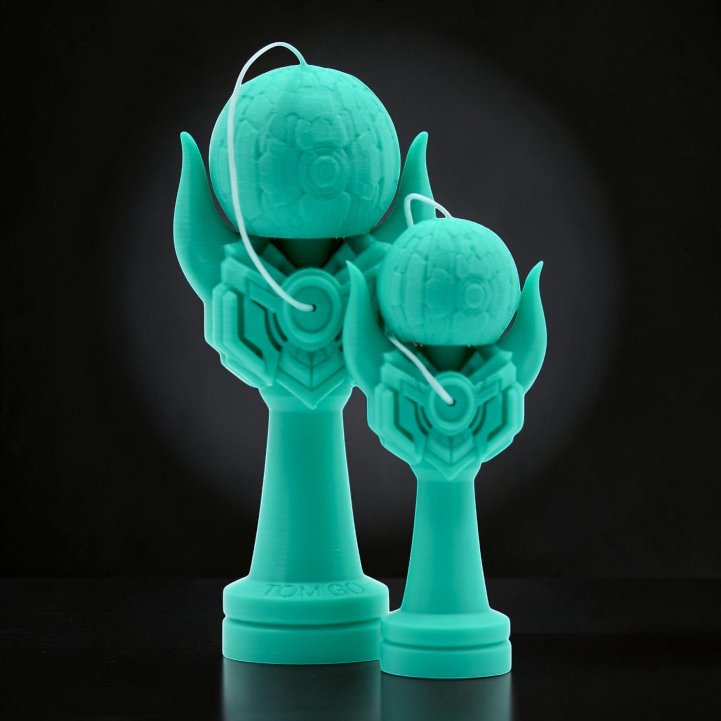 Tom GO Kendama Geeker Iron M in teal, featuring a unique armored design with intricate details on the cup and tama. Two sizes shown.