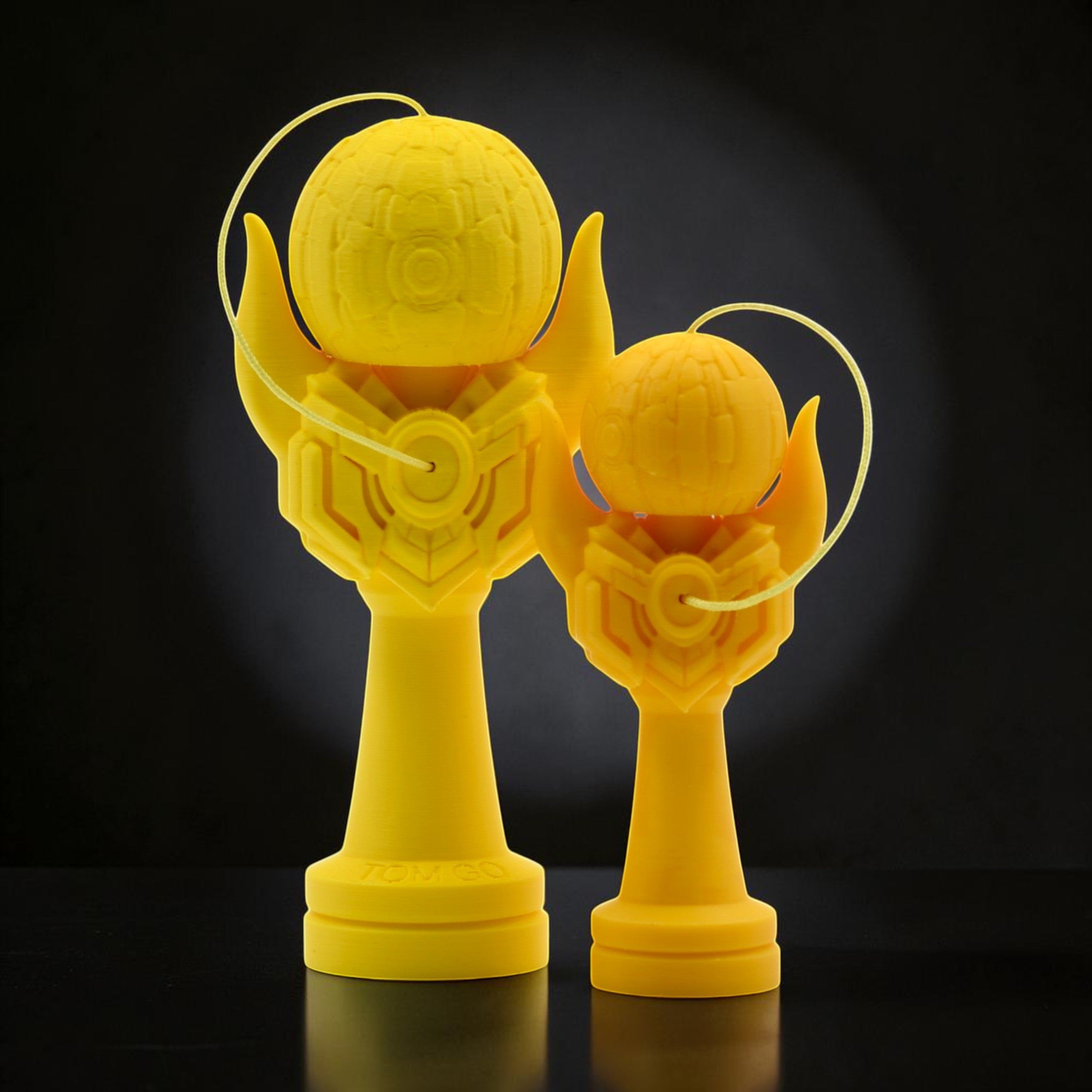 Tom GO Kendama Geeker Iron M, a bright yellow kendama toy with a unique, armored design. Two sizes shown.