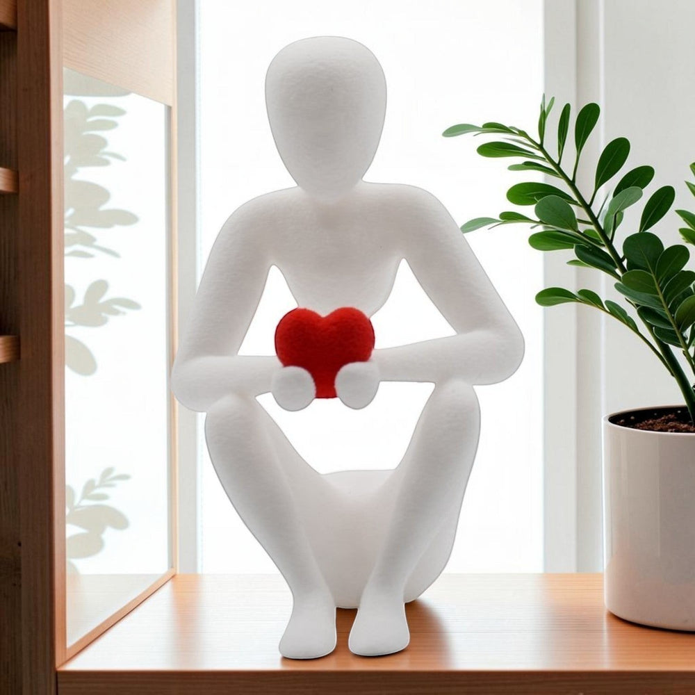 Tom GOH abstract white figurine holding a red heart, seated contemplative pose, minimalist decor.