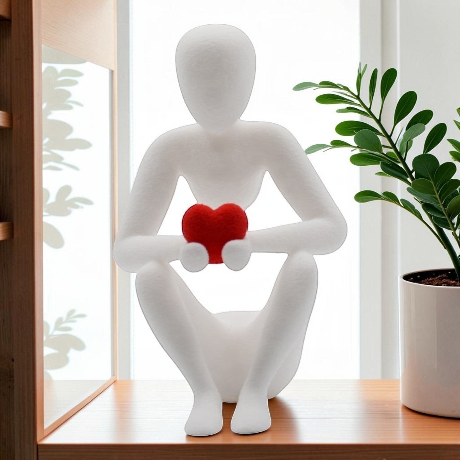 Tom GOH abstract white figurine holding a red heart, seated contemplative pose, minimalist decor.